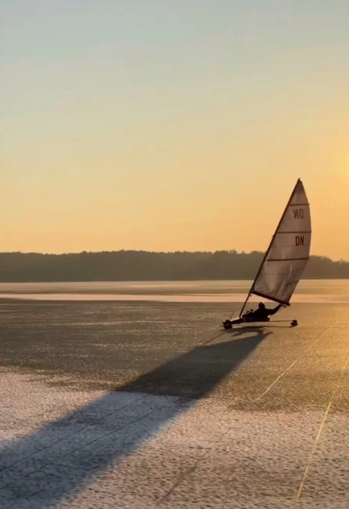 Jednoosobowy lodowy jacht żaglowy sunie po zamarzniętym jeziorze o zachodzie słońca